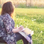 woman looking over a green field while writing