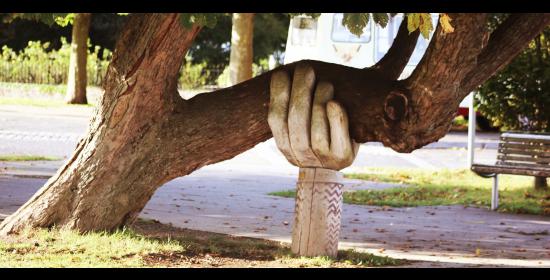 a carved wooden hand coming out of the ground is holding up the trunk of a tree