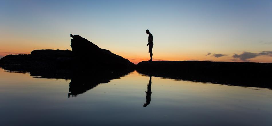 man standing looking at reflection in water